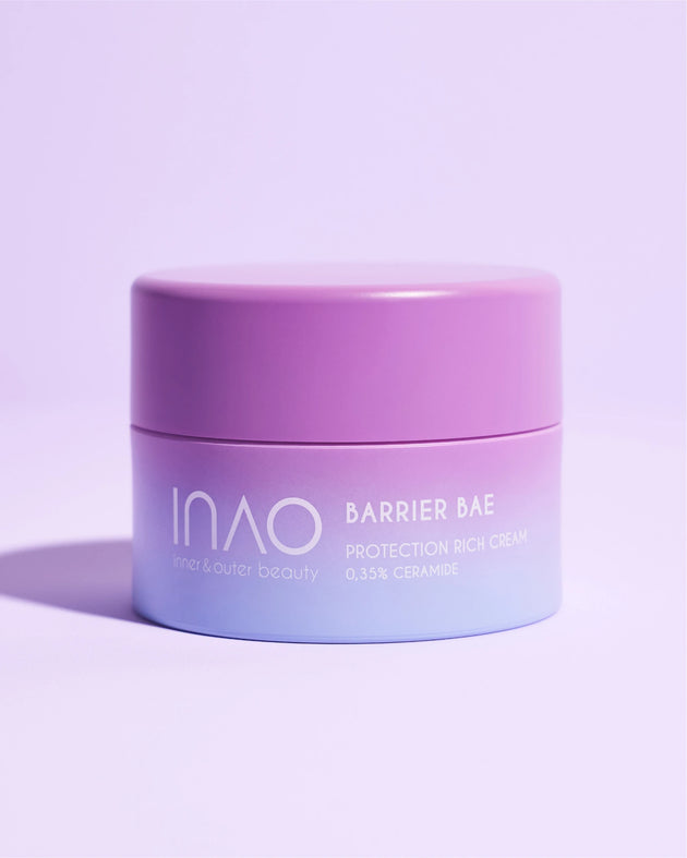 Ein pastellviolett-blauer Tiegel mit der Barrier Bae Protection Rich Cream von INAO by essence, angereichert mit Ceramid für eine gesunde Hautbarriere, steht auf einer hellvioletten Oberfläche und wirft einen weichen Schatten auf einen minimalistischen Hintergrund.