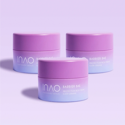 Drei violette und lavendelfarbene Tiegel der Barrier Bae Protection Rich Cream von INAO by essence sind auf einem hellvioletten Hintergrund angeordnet, wobei die Etiketten Ceramide für eine starke Hautbarriere hervorheben.
