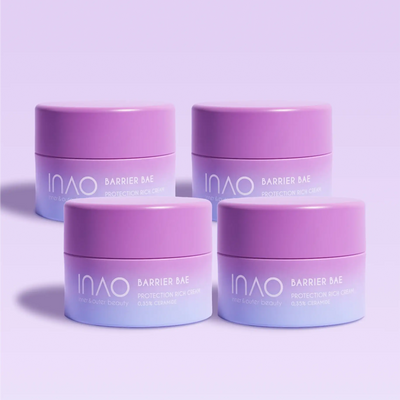 Vier violette und lavendelfarbene Tiegel der Barrier Bae Protection Rich Cream von INAO by essence sind auf einem hellvioletten Hintergrund angeordnet, wobei sanfte Schatten unter jedem Tiegel die hautbarrierestärkende Formel hervorheben.