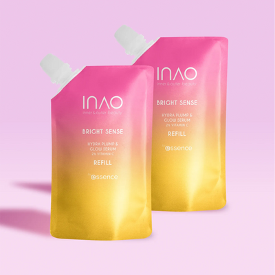 Zwei rosa und gelbe Nachfüllbeutel mit Farbverlauf und der Aufschrift „Bright Sense Hydra Plump & Glow Serum Refill“ von INAO by essence stehen auf einem hellrosa Untergrund und werfen Schatten.