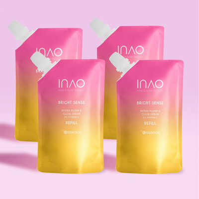 Vier rosa und gelbe Nachfüllbeutel mit Farbverlauf und der Aufschrift „INAO by essence Bright Sense Hydra Plump & Glow Serum Refill“ sind vor einem hellrosa Hintergrund angeordnet.