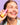 Eine lächelnde Frau hält eine Flasche INAO von essence Bright Sense Hydra Plump & Glow Serum vor ihr Gesicht, mit einem Tropfen Serum auf ihrer Wange, vor einem hellvioletten gefliesten Hintergrund.