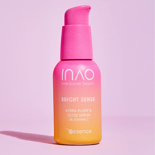 Eine Flasche INAO by essence Bright Sense Hydra Plump & Glow Serum mit 2 % Vitamin C und Hyaluronsäure in einem rosa-orangefarbenen Farbverlauf steht auf einem hellrosa Hintergrund und verfügt über einen Pumpspender.