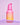 Eine Flasche INAO von essence Bright Sense Hydra Plump & Glow Serum mit Farbverlauf in Rosa und Orange und einem Pumpspender erscheint vor einem hellrosa Hintergrund mit violettem Akzent.