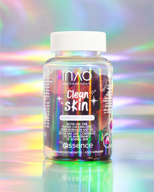 Eine Flasche der Clean Skin Community Edition Gummies von INAO by essence, angereichert mit Biotin, Zink und Ceramid, steht vor einem pastellfarbenen, schillernden Hintergrund. Das Etikett zeigt Sterne, farbenfrohe Details sowie englischen und deutschen Text.