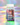 Eine Flasche der Clean Skin Community Edition Gummies von INAO by essence, angereichert mit Biotin, Zink und Ceramid, steht vor einem pastellfarbenen, schillernden Hintergrund. Das Etikett zeigt Sterne, farbenfrohe Details sowie englischen und deutschen Text.