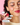 Eine Frau mit rotem Lippenstift hält ein rotes Clean Skin x JUICY BOMB Gummy von INAO von essence. Textblasen heben Vitamin C, Biotin & Zink sowie Ceramid aus Reiskleieextrakt hervor. Der Hintergrund ist rosa.