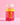 Eine durchsichtige Plastikflasche mit der Aufschrift „Clean Skin x JUICY BOMB Gummies“ von INAO by essence, gefüllt mit leuchtend rosa Gummibärchen, reich an Biotin und Zink, steht auf einer rosa Fläche mit rosa Hintergrund. Das Etikett hat gelb-rosa Text und einen weißen Verschluss.