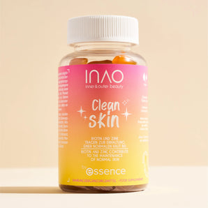 Eine Flasche INAO by essence Clean Skin Gummies mit weißem Verschluss enthält orangefarbene Gummibärchen. Das rosa-gelbe Etikett trägt weißen Text, und die Flasche steht auf einer beigen Fläche mit beigem Hintergrund.