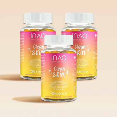 Drei Flaschen INAO von essence Clean Skin Gummies mit rosa, orangefarbenen und gelben Farbverlaufsetiketten mit den Inhaltsstoffen Biotin, Zink und Ceramid sowie Glitzer werden auf einem hellbeigen Hintergrund präsentiert.