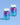 Zwei Flaschen INAO by essence Dream & Chill Gummies sind vor einem hellblauen Hintergrund mit Farbverlauf abgebildet. Die Flaschen haben weiße Deckel, blau-violette Etiketten mit weißem Text sowie Stern- und Mondverzierungen.