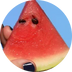 Eine Hand mit dunkel lackierten Nägeln hält ein Stück Wassermelone vor blauem Hintergrund. Zwei Wassermelonenkerne sind so angeordnet, dass sie wie Augen aussehen und der Frucht ein gesichtsähnliches Aussehen verleihen.