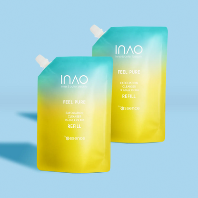 Zwei Nachfüllbeutel mit Farbverlauf in Gelb und Blau des INAO by essence Feel Pure AHA & BHA Exfoliation Cleanser Refill mit weißen Kappen stehen aufrecht auf einem hellblauen Hintergrund.