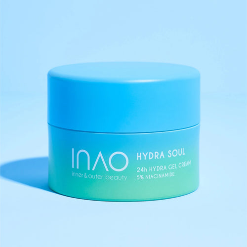 Auf einem passenden blauen Hintergrund steht ein blau-grüner Tiegel mit der Aufschrift „Hydra Soul 24h Hydra Gel Cream“ von INAO by essence. Diese Gelcreme mit Niacinamid spendet 24 Stunden Feuchtigkeit für innere und äußere Schönheit.