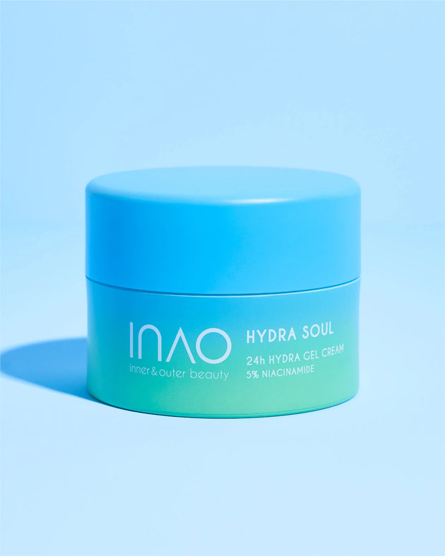 Auf einem passenden blauen Hintergrund steht ein blau-grüner Tiegel mit der Aufschrift „Hydra Soul 24h Hydra Gel Cream“ von INAO by essence. Diese Gelcreme mit Niacinamid spendet 24 Stunden Feuchtigkeit für innere und äußere Schönheit.