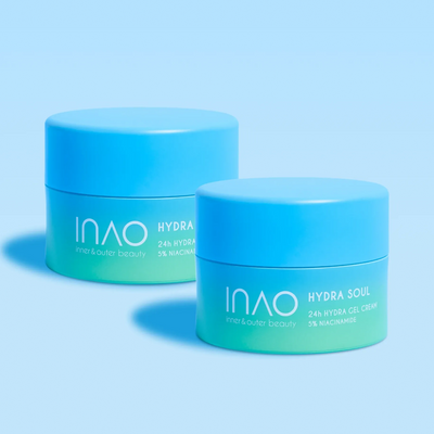 Zwei blaue Tiegel der INAO by essence Hydra Soul 24h Hydra Gel Cream sind auf hellblauem Untergrund mit passendem Hintergrund abgebildet. Die Etiketten auf der Vorderseite tragen den Schriftzug „24h Feuchtigkeit“ und beide Produktnamen sind deutlich sichtbar.