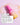 Eine leuchtend pink-gelbe Pumpflasche mit der Aufschrift „Happy Mornings mit INAO“ von INAO by essence liegt auf einer pfirsichfarbenen Oberfläche, umgeben von Serum – perfekt für die tägliche Routine. Die deutsche Gebrauchsanweisung befindet sich in einer weißen Box.