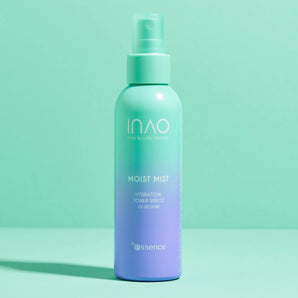 Ein blaugrüner und lavendelfarbener INAO von essence Moist Mist Hydration Toner Spritz steht aufrecht auf einer pastellfarbenen Oberfläche und hebt die feuchtigkeitsspendende Kraft von Betain vor einem minimalistischen Hintergrund in Blaugrün und Mintgrün hervor.