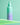 Eine grün-violette Flasche INAO by essence Moist Mist Hydration Toner Spritz mit 2 % Betain für erfrischende Feuchtigkeitsversorgung steht auf einem leuchtend grünen Regal vor einem grünen Hintergrund.