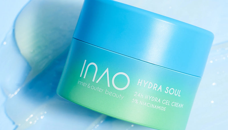 Auf einem blauen Untergrund ist ein blau-grüner Tiegel der INAO Hydra Soul 24h Hydra Gel Cream mit 5% Niacinamid abgebildet, daneben ist Creme aufgestrichen, in der Ecke ist das „essence“-Logo zu sehen.