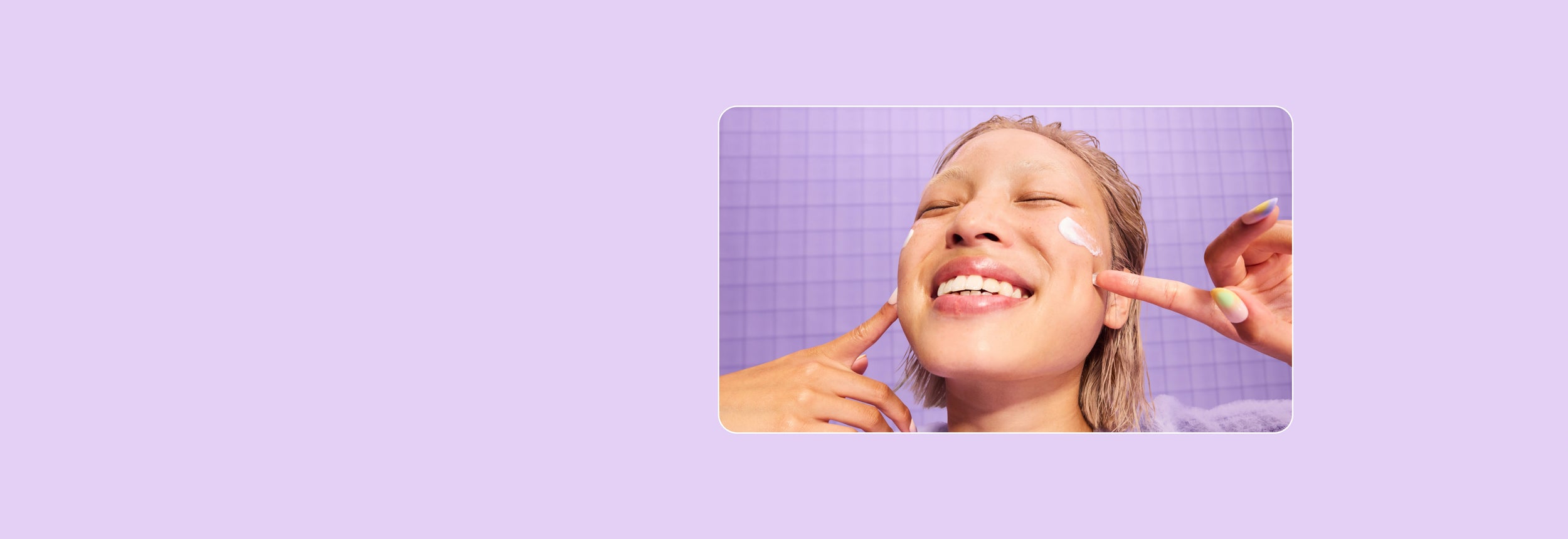 Eine lächelnde Person mit nassen Haaren trägt mit beiden Händen Creme auf ihre Wangen auf. Sie steht vor einem lila gekachelten Hintergrund. Das Bild zeigt unten rechts das Logo „essence“.