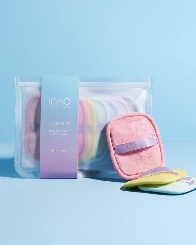 Ein transparenter Beutel mit lavendelfarbenem Etikett von INAO by essence enthält mehrere pastellfarbene Swipe Tribe Reusable Makeup Remover Pads. Drei Pads liegen außen auf einer hellblauen Oberfläche und sorgen für saubere Haut.