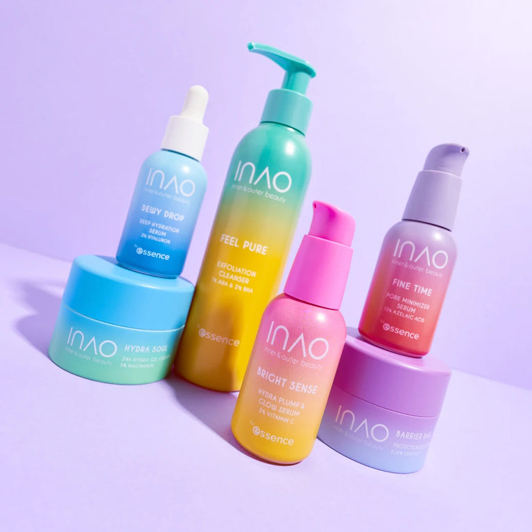 Fünf farbenfrohe INAO-Hautpflegeprodukte, darunter Flaschen mit Pumpen und Tropfkappen sowie zwei runde Tiegel, sind auf einer hellvioletten Oberfläche mit passendem hellvioletten Hintergrund angeordnet.