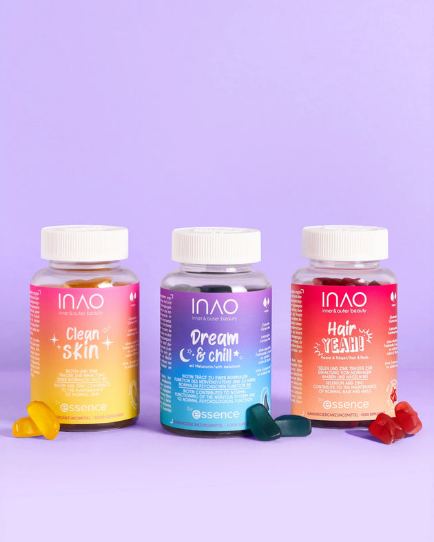 Drei bunte Flaschen aus dem INAO by essence Supplement Lover Sparset - "Clean Skin Gummies", "Dream & Chill" und "Hair YEAH! Gummies" - stehen nebeneinander auf einem lilafarbenen Hintergrund, vor dem jeweils passende Gummibärchen verstreut sind.