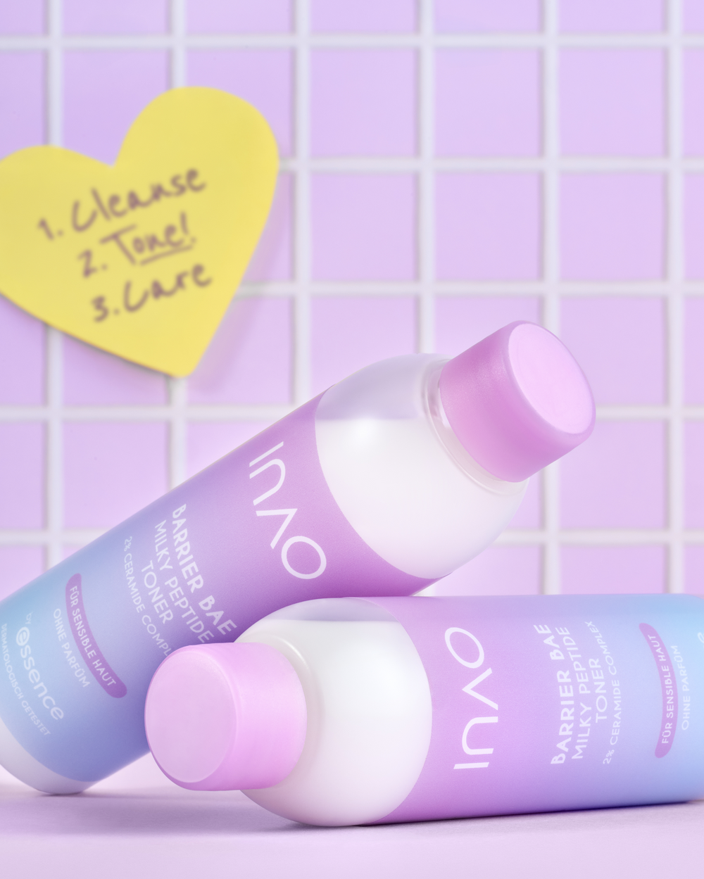 Zwei Flaschen des Barrier Bae Milky Peptide Toner liegen vor lila Fliesen neben einem herzförmigen Notizzettel mit den Schritten „1. Cleanse, 2. Tone, 3. Care“.