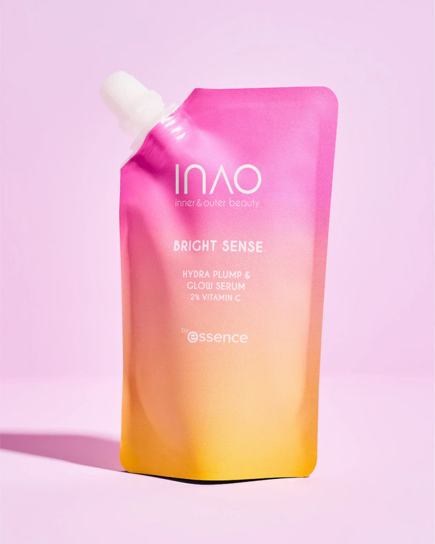 Auf einem rosa Hintergrund steht aufrecht ein rosa-gelber Farbverlaufsbeutel mit der Aufschrift „INAO by essence, Bright Sense Hydra Plump & Glow Serum Refill“ mit Hyaluronsäure.