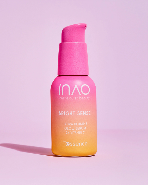 Eine Flasche INAO by essence Bright Sense Hydra Plump & Glow Serum mit 2 % Vitamin C und Hyaluronsäure in einem rosa-orangefarbenen Farbverlauf steht auf einem hellrosa Hintergrund und verfügt über einen Pumpspender.