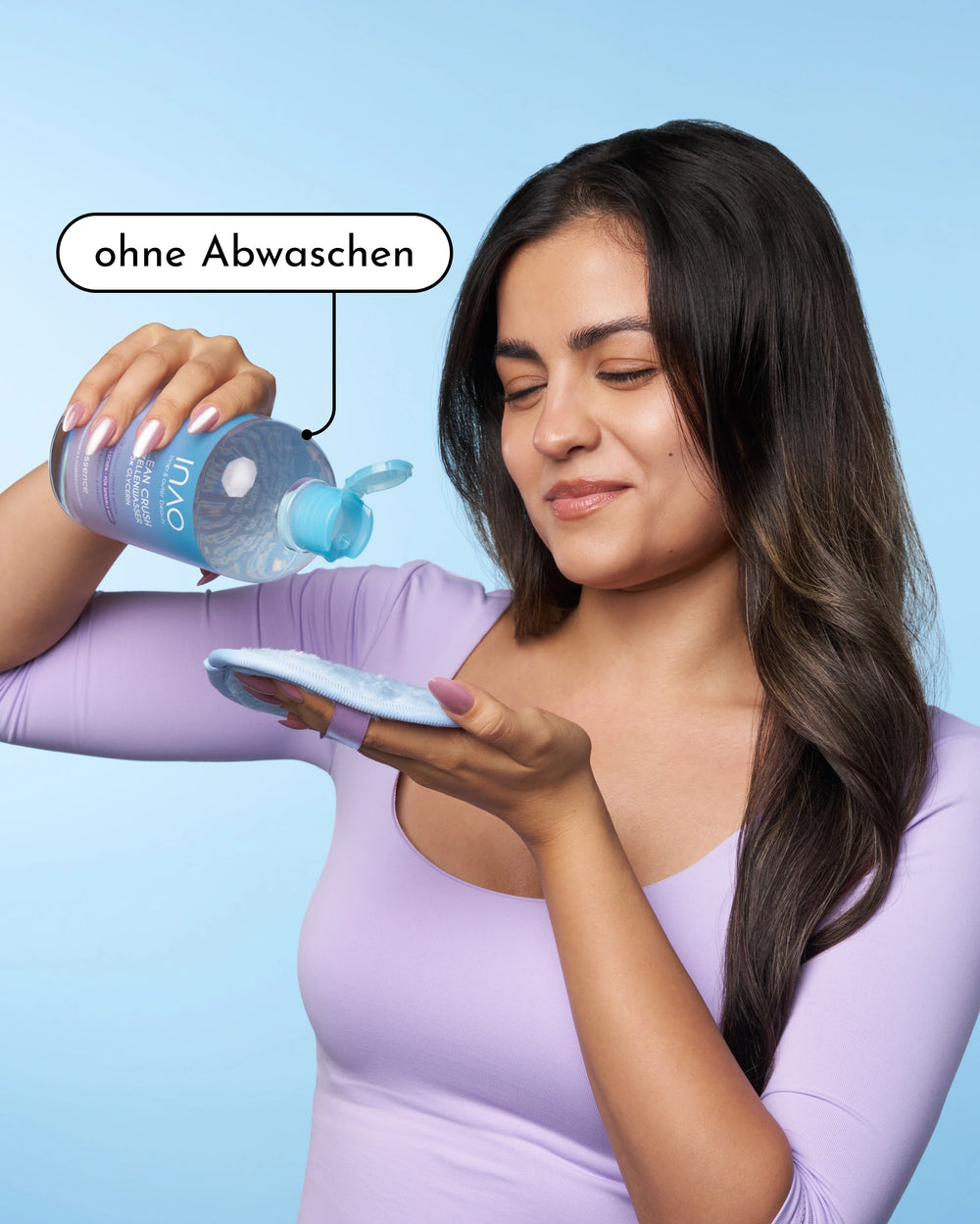 Eine Frau in einem lavendelfarbenen Oberteil lächelt, während sie INAO by essence Clean Crush Mizellenwasser auf ein Wattepad schüttet. In einer Sprechblase steht "ohne Abwaschen". Der Hintergrund ist einfarbig hellblau.