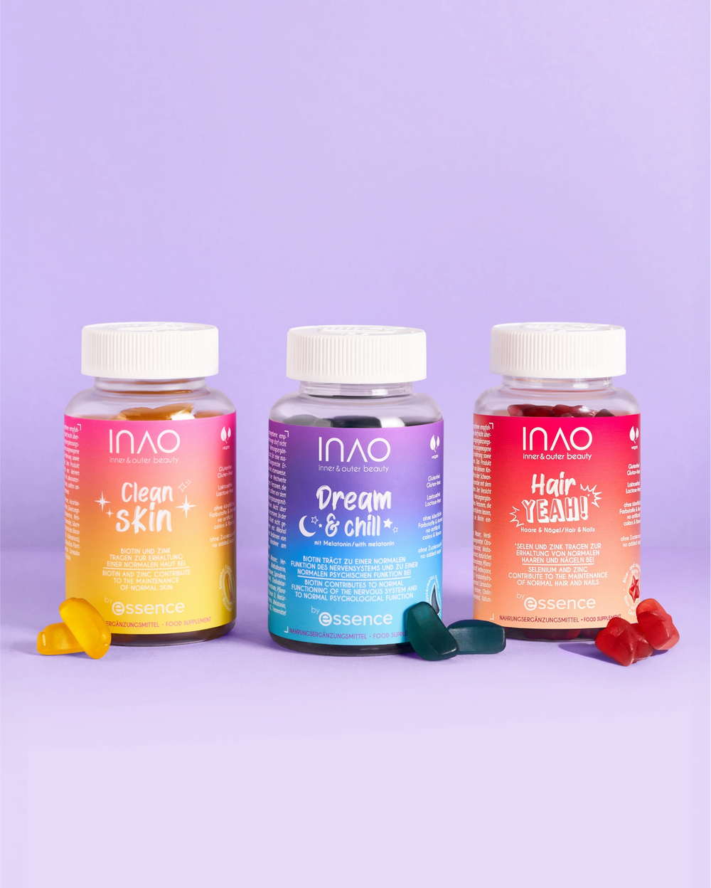 Drei farbenfrohe Flaschen mit INAO by essence Clean Skin Gummies, Dream & Chill und Hair Yeah sind vor einem violetten Hintergrund angeordnet, jeweils mit passenden Haut Vitamine Gummibonbons davor.