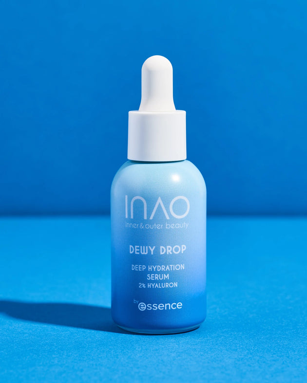 Eine Flasche Dewy Drop Deep Hydration Serum von INAO by essence mit blauem Farbverlauf und 2 % Hyaluron für tiefe Feuchtigkeitsversorgung sowie einem weißen Tropfverschluss steht auf einer blauen Fläche vor blauem Hintergrund.