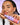 Eine Frau mit geflochtenen Haaren lächelt sanft, während sie vor einem violetten Rasterhintergrund eine violette Flasche mit der Aufschrift „Fine Time Daily Hypo Spray“ von INAO by essence in der Hand hält und so dieses Gesichtsspray hervorhebt, das die Haut beruhigt.