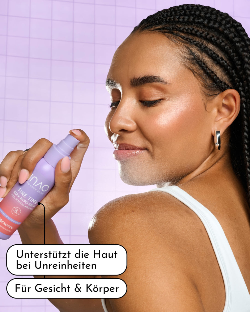 Eine Frau mit geflochtenen Haaren sprüht sich „Fine Time Daily Hypo Spray“ von INAO by essence ins Gesicht und lächelt dabei mit geschlossenen Augen. Text auf Deutsch: „Unterstützt die Haut bei Unreinheiten. Beruhigt die Haut. Für Gesicht & Körper.“ Hinter ihr ist ein lavendelfarbener Fliesenhintergrund zu sehen.