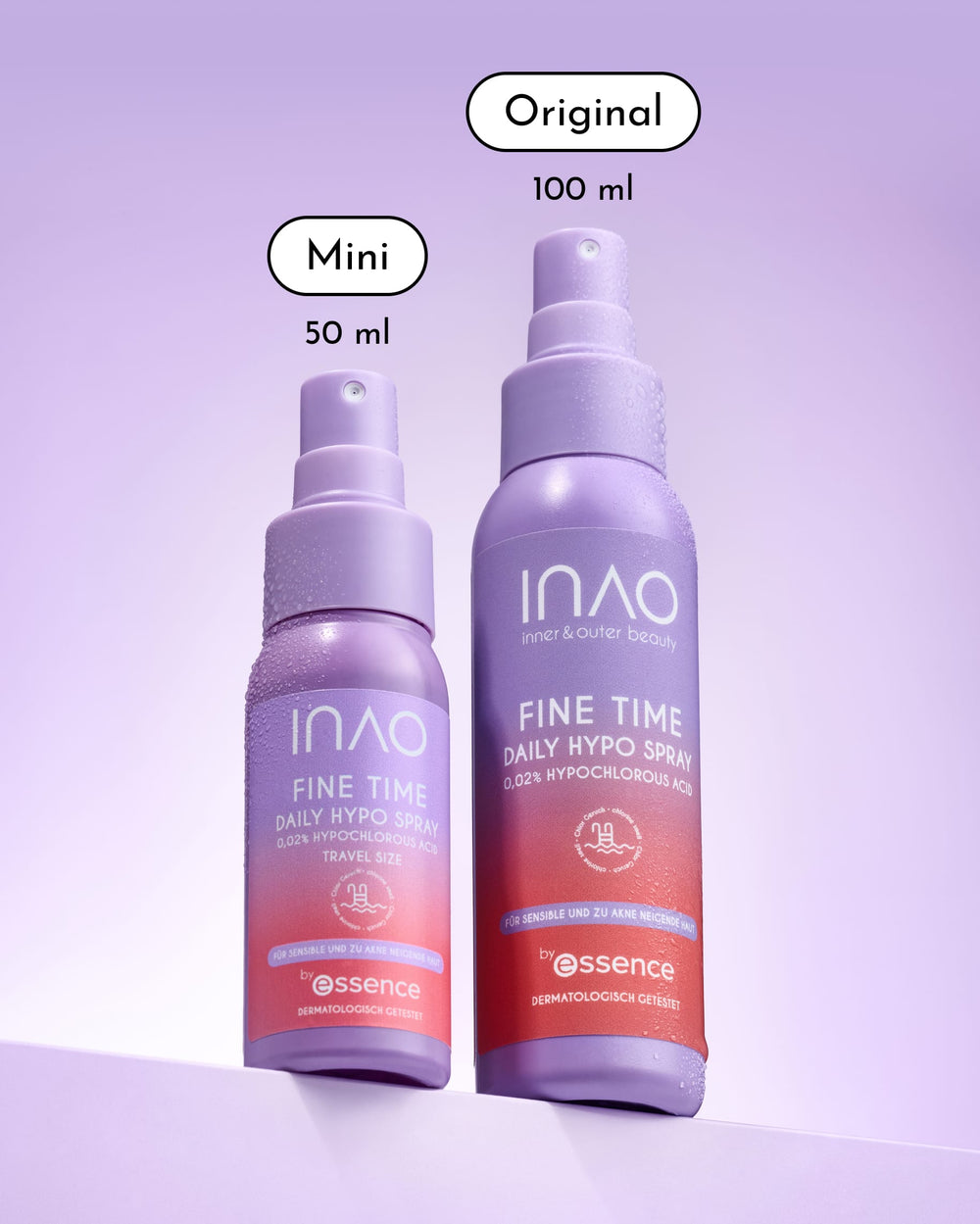 Zwei violette Sprühflaschen mit der Aufschrift „Fine Time Daily Hypo Spray“ von INAO by essence stehen aufrecht. Die linke Flasche fasst 50 ml (Mini), die rechte 100 ml (Original). Beide weisen Kondenswasser auf und sind vor einem lavendelfarbenen Hintergrund mit Farbverlauf abgebildet. Dieses sanfte hypochlorige Gesichtsspray beruhigt die Haut bei jeder Anwendung.