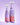 Zwei violette Sprühflaschen mit der Aufschrift „Fine Time Daily Hypo Spray“ von INAO by essence stehen aufrecht. Die linke Flasche fasst 50 ml (Mini), die rechte 100 ml (Original). Beide weisen Kondenswasser auf und sind vor einem lavendelfarbenen Hintergrund mit Farbverlauf abgebildet. Dieses sanfte hypochlorige Gesichtsspray beruhigt die Haut bei jeder Anwendung.