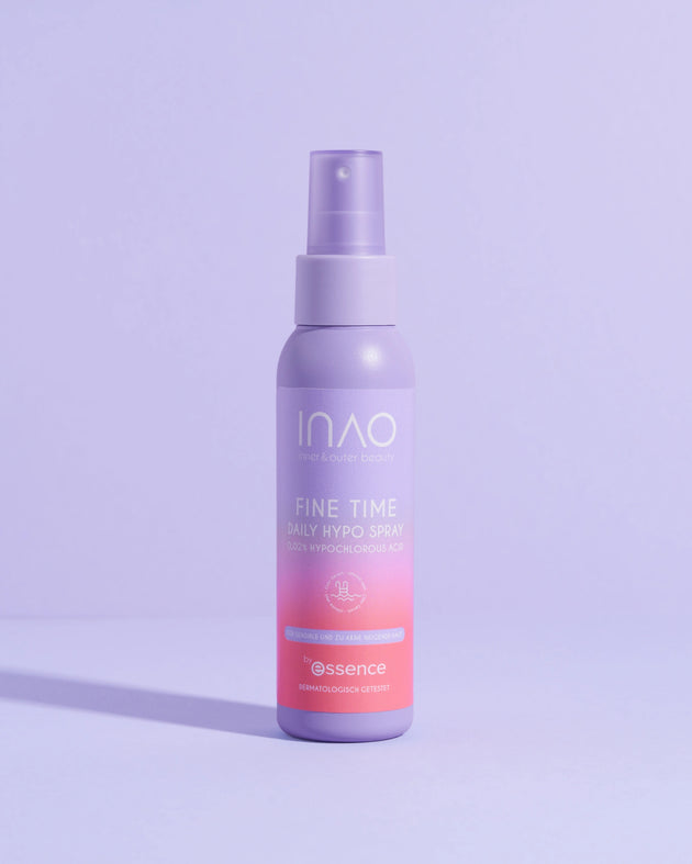 Eine violette Flasche Fine Time Daily Hypo Spray von INAO by essence (0,025% hypochlorige Säure) steht aufrecht auf einer violetten Fläche und wirft einen Schatten auf einen hellvioletten Hintergrund.