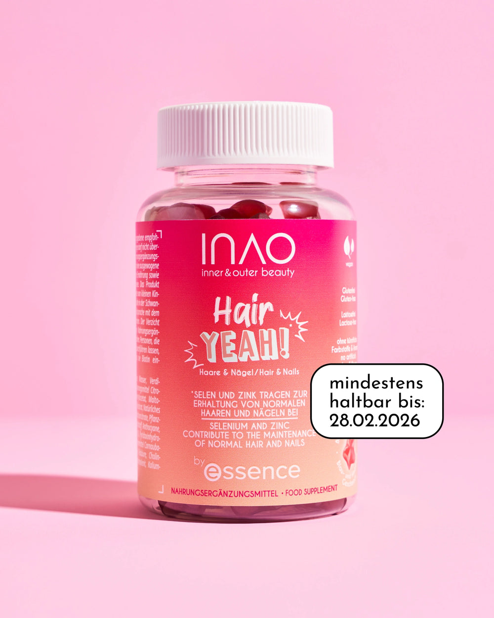 Eine Flasche INAO by essence Hair YEAH! Gummies für Haare und Nägel ruht auf einem rosa Hintergrund. Das rosa-weiße Etikett ist sichtbar und zeigt das Verfallsdatum an: "mindestens haltbar bis: 28.02.2026".