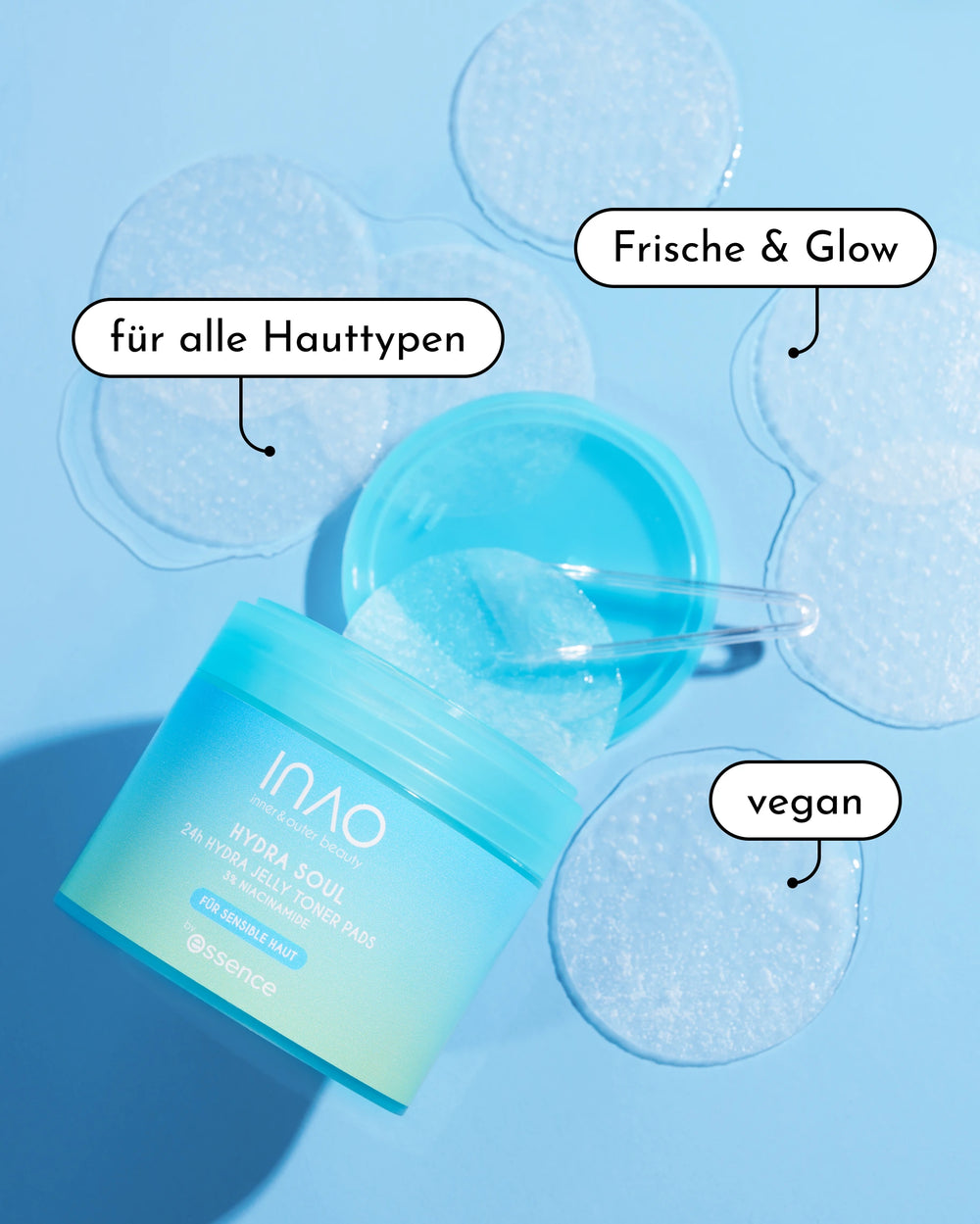 Ein geöffneter blauer Tiegel mit INAO by essence Hydra Soul 24h Hydra Jelly Toner Pads steht mit einem durchsichtigen Spatel auf dem Deckel, umgeben von runden Pads. Die Etiketten lauten: "für alle Hauttypen", "Feuchtigkeit & Glow" und "vegan".