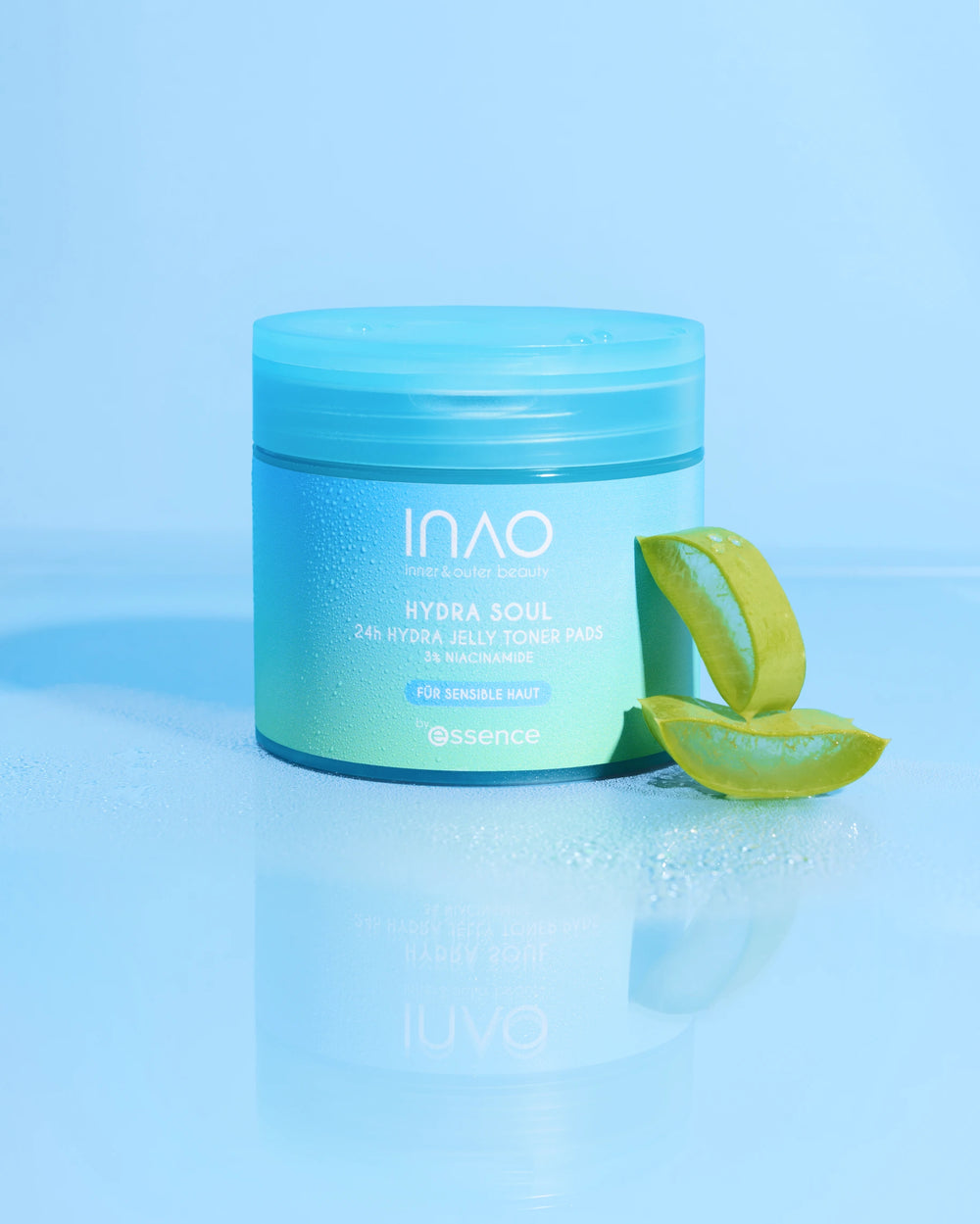 Ein blaugrüner Tiegel der INAO by essence Hydra Soul 24h Hydra Jelly Toner Pads ruht auf einer glänzenden Oberfläche neben Aloe Vera Blättern, wobei ein hellblauer Hintergrund die frische und feuchtigkeitsspendende Ausstrahlung hervorhebt.