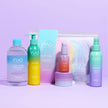 Das Happy Evenings Sparset von INAO by essence enthält farbenfrohe Hautpflegeprodukte - Hydration Toner, Flaschen, Pumpspender, Tiegel und einen Beutel mit Regenbogen-Makeup-Entferner-Pads - die alle auf einer lila Oberfläche mit hellviolettem Hintergrund präsentiert werden.