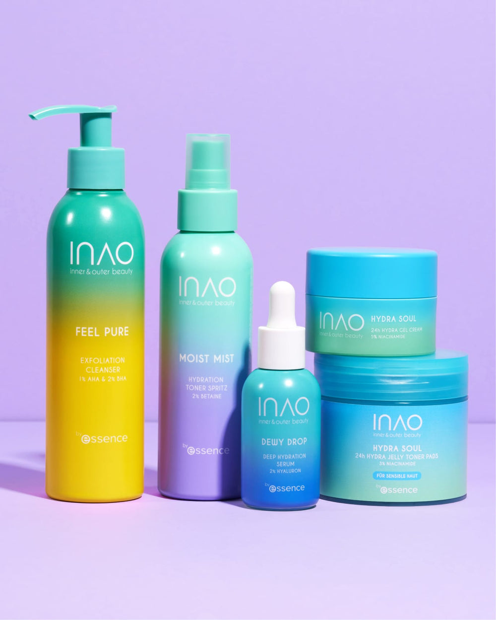 Fünf farbenfrohe INAO by essence Produkte, darunter das Happy Moisture Sparset, sind auf einer lilafarbenen Fläche angeordnet; tealfarbene, blaue und gelbe Flaschen tragen Namen wie "Feel Pure", "Moist Mist" und "Hydra Soul".