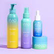 Vier farbenfrohe INAO by essence Happy Moisture Sparset-Produkte – Peeling-Reiniger, Toner-Spray, Serum und Gel-Creme – liegen auf einer violetten Oberfläche. Ihre Verpackung in den Farbverläufen Blau, Grün und Gelb betont die intensive Feuchtigkeitsversorgung.