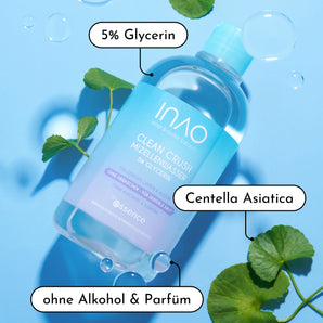 Eine Flasche INAO by essence New Drop Sparset Micellar Water ruht auf einer blauen Fläche mit Centella Asiatica Blättern und Blasen - auf dem Etikett stehen "5% Glycerin", "sanfte Reinigung", "Centella Asiatica" und das New Drop Sparset.