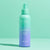 Ein blaugrüner und lavendelfarbener INAO von essence Moist Mist Hydration Toner Spritz steht aufrecht auf einer pastellfarbenen Oberfläche und hebt die feuchtigkeitsspendende Kraft von Betain vor einem minimalistischen Hintergrund in Blaugrün und Mintgrün hervor.
