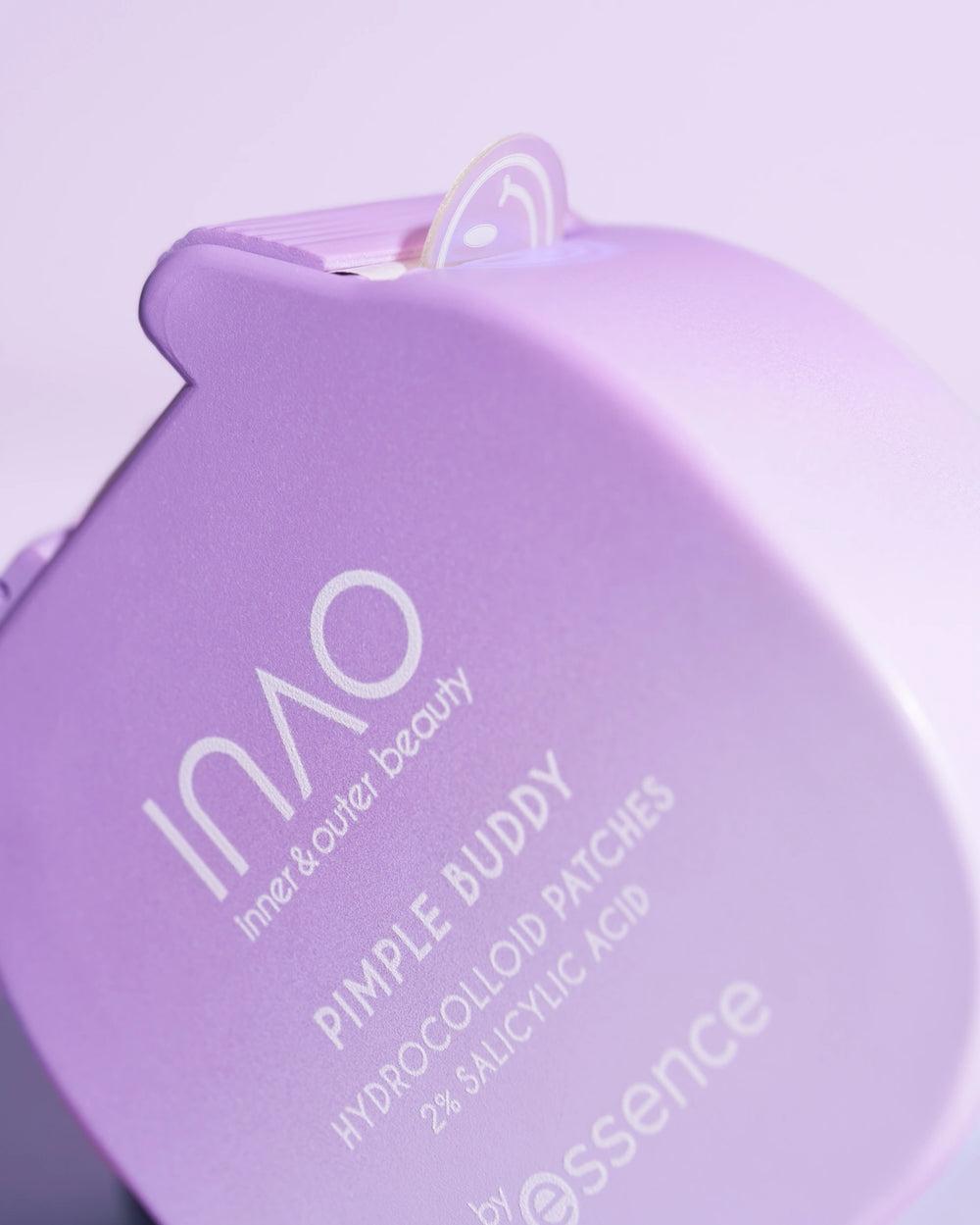 Nahaufnahme eines pastellvioletten Behälters mit der Aufschrift "Pimple Buddy Hydrocolloid Patches" von INAO by essence, wobei ein Pflaster an der Oberseite teilweise sichtbar ist.