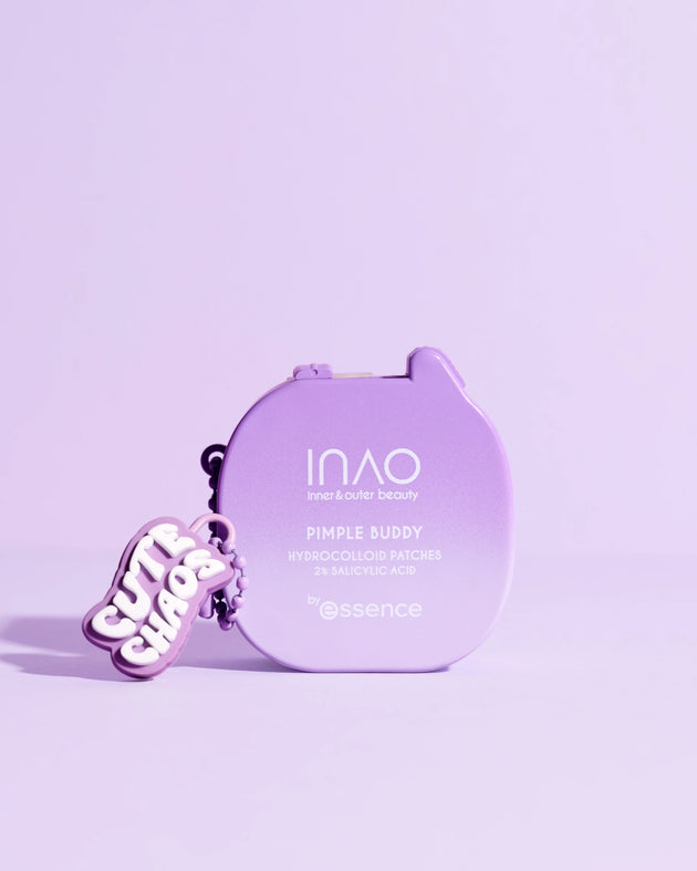 Ein lavendelfarbener Behälter mit der Aufschrift "Pimple Buddy Hydrocolloid Patches" von INAO by essence steht auf einer pastellfarbenen lila Fläche, die mit einem "Cute Chaos"-Schlüsselanhänger geschmückt ist, und das alles in einem zart lila gehaltenen Rahmen.