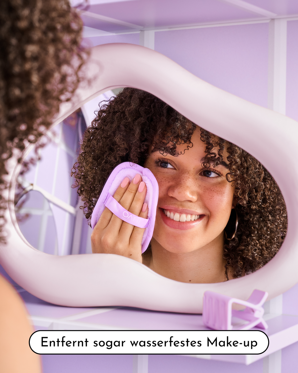 Lächelnde Person mit lockigem Haar entfernt Make-up mit einem lila Make-up-Entferner-Pad, mit dem Hinweis „Entfernt sogar wasserfestes Make-up“.